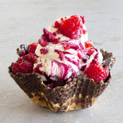 A photo of a vanilla raspberry ice cream in a chocolate waffle cup.