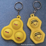 Photo of a Chicky Pop-It (a three bubble pop-it with cute chicky faces on each), and a Buzzy Bee Pop-It (a two bubble pop-it with cute bees on each bubble). Photo by pinchiegram.